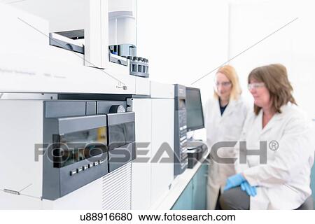 Stock Image - Female scientists at workstation testing oil samples. Fotosearch