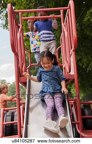 Stock Photo - Four boys and girls sliding on playground slide. Fotosearch