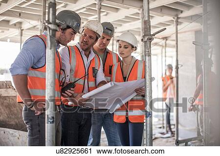 Stock Image - Four female and male builders with blueprint on construction site. Fotosearch