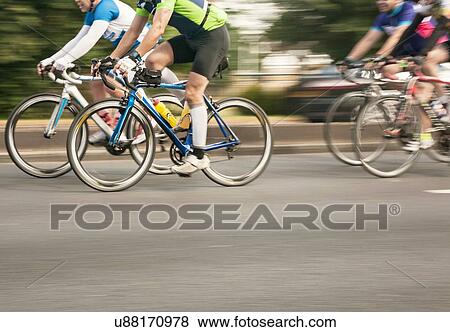 Stock Photo - Four racing cyclists speeding on urban road in racing cycle race. Fotosearch