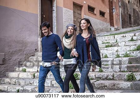 Stock Photo - Friends walking down stone steps arm in arm smiling. Fotosearch
