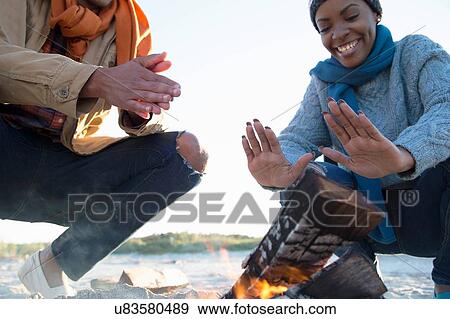 Stock Photo - Friends warming hands over camp fire. Fotosearch
