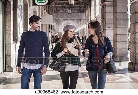 Stock Image - Front view of friends walking side by side in shopping mall smiling. Fotosearch