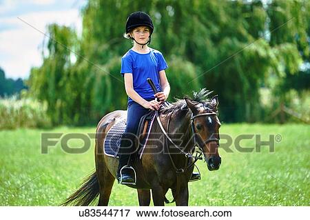 Stock Photo - Front view of girl on horseback wearing riding hat looking at camera smiling. Fotosearch