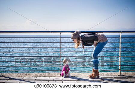 Full length side view of young woman by railings in front of ocean bending over looking at dog View Large Photo Image Stock Image - Full length side view of young woman by railings in front of ocean bending over looking at dog. Fotosearch