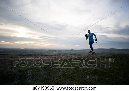 Stock Photo - Full length view of fell runner running against dramatic sky. Fotosearch