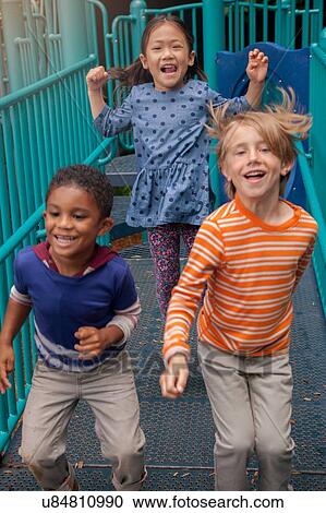Stock Image - Girl and boys running on playground climbing frame. Fotosearch