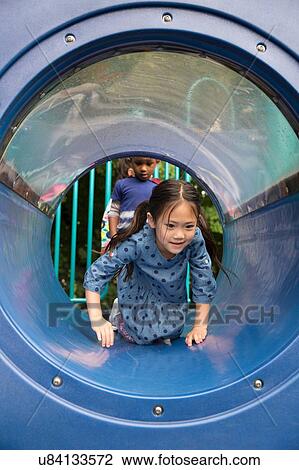 Stock Image - Girl crawling along playground tunnel. Fotosearch
