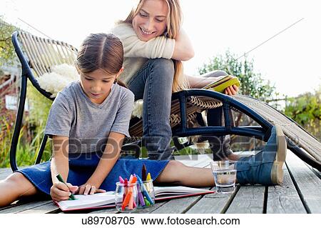 Stock Photography - Girl drawing on decking with mother sitting close by, smiling. Fotosearch