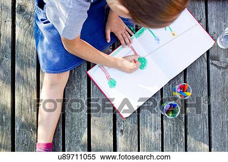 Stock Photography - Girl drawing picture in notebook, high angle. Fotosearch