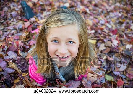 Picture - Girl lying on autumn leaves in garden. Fotosearch