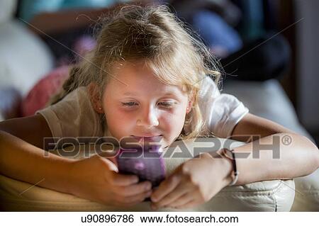 Stock Photograph - Girl lying on front using a smartphone. Fotosearch