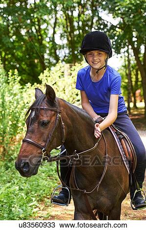 Stock Image - Girl on horse wearing riding hat looking at camera smiling. Fotosearch