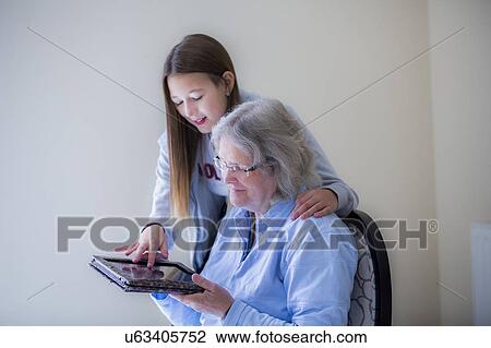 Stock Image - Girl showing grandmother tablet. Fotosearch