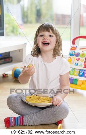 Stock Image - Girl sitting on floor eating french fries. Fotosearch