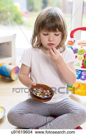 Picture - Girl sitting on floor with bowl of sweets. Fotosearch