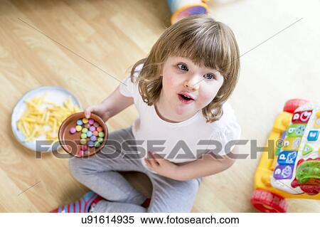 Stock Photography - Girl sitting on floor with bowl of sweets. Fotosearch