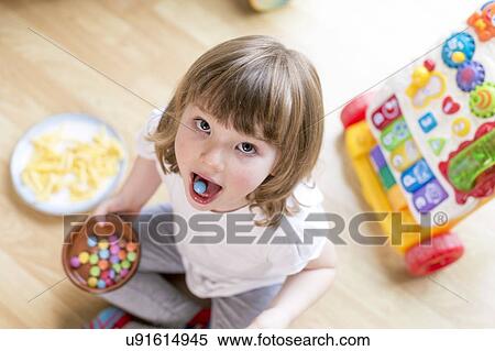 Stock Photography - Girl sitting on floor with bowl of sweets. Fotosearch