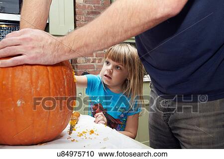 Stock Image - Girl watching father scooping out pumpkin. Fotosearch