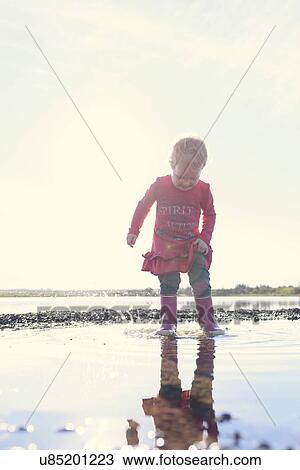 Stock Image - Girl wearing rubber boots splashing in lake, Hafravatn, Iceland. Fotosearch