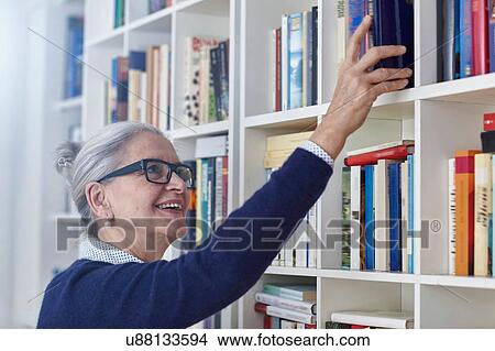 Happy grey haired mature woman selecting book from bookshelves View Large Photo Image Picture - Happy grey haired mature woman selecting book from bookshelves. Fotosearch