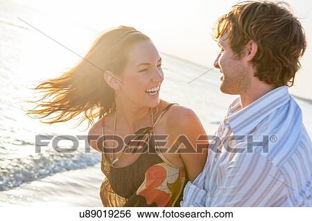 Stock Photograph - Happy young couple laughing on sunlit beach, Majorca, Spain. Fotosearch