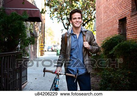 Happy young man strolling with cycle on sidewalk View Large Photo Image Stock Photo - Happy young man strolling with cycle on sidewalk. Fotosearch