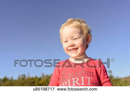 Stock Photo - Head and shoulder portrait of cute girl against blue sky. Fotosearch