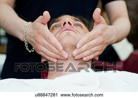 Stock Image - Head and shoulders of young man, head back, having facial massage. Fotosearch