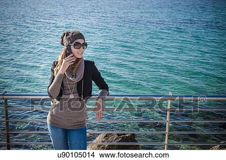Picture - High angle view of young woman leaning against railings using smartphone smiling. Fotosearch