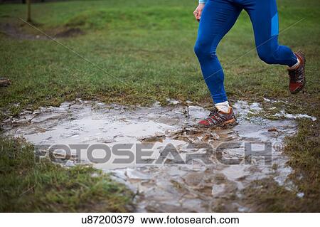 Stock Photo - Legs of runner running through muddy puddle. Fotosearch