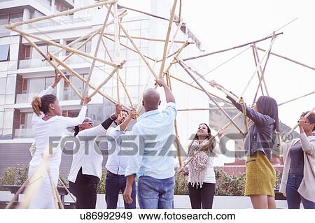 Stock Photo - Low angle view of colleagues in team building task lifting building wooden structure. Fotosearch