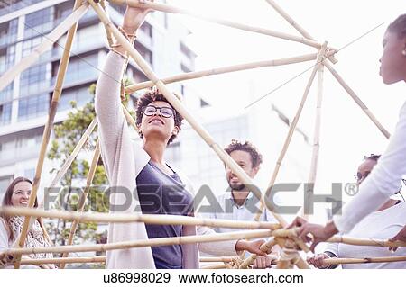 Stock Photo - Low angle view of colleagues in team building task building wooden structure. Fotosearch