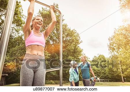 Stock Photo - Low angle view of mature woman doing pull ups in park smiling. Fotosearch