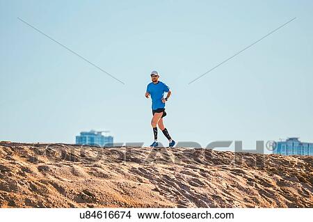 Picture - "Low angle view of mid adult man running on sand dune, Dubai, United Arab Emirates". Fotosearch