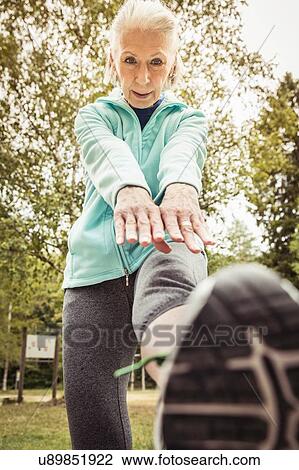 Stock Image - Low angle view of senior woman bending forward touching toes. Fotosearch