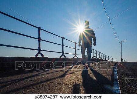 Low angle view of silhouetted man strolling on promenade View Large Photo Image Stock Photo - Low angle view of silhouetted man strolling on promenade. Fotosearch