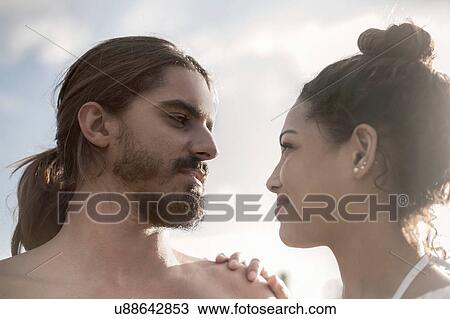 Stock Image - Low angle view of young couple face to face smiling. Fotosearch