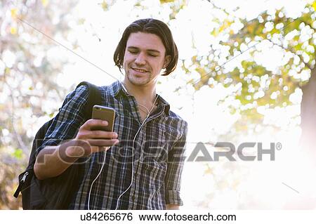 Stock Photograph - Low angle view of young man holding smartphone looking down smiling. Fotosearch