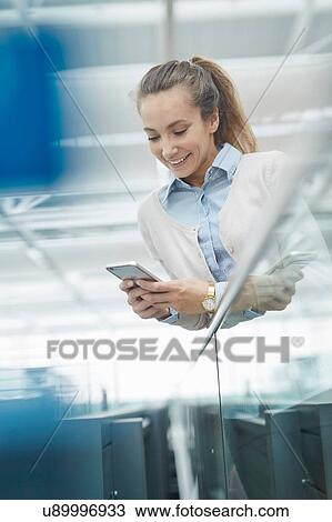 Stock Image - Low angle view of young woman looking down using smartphone smiling. Fotosearch