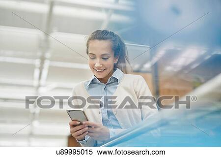 Stock Photography - Low angle view of young woman looking down using smartphone smiling. Fotosearch