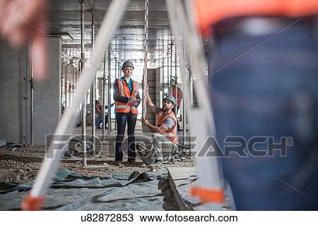 Stock Image - Male and female builders taking measurements for surveyor. Fotosearch