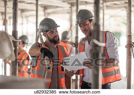 Stock Photography - Male builders looking at blueprint on construction site. Fotosearch
