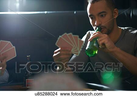 Picture - Male friends drinking beer and playing card game at pub card table. Fotosearch