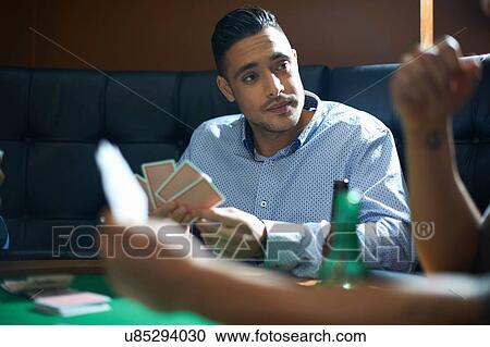 Stock Image - Male friends playing card game at pub card table. Fotosearch