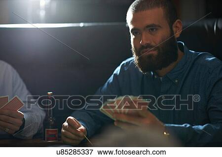 Stock Photo - Male friends playing card game at traditional uk pub. Fotosearch