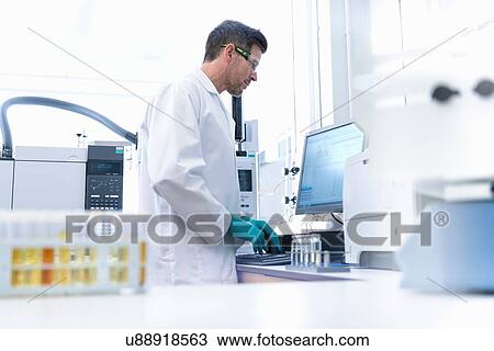 Stock Image - Male scientist at workstation testing oil samples. Fotosearch