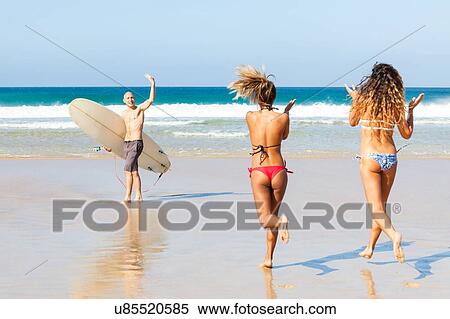 Stock Photography - Male surfer waving to female friends on beach, El Cotillo, Fuerteventura, Spain. Fotosearch