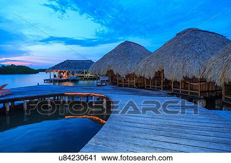 Stock Image - "Male tourists in distant waterfront chalet at dusk, St. Georges Caye, Belize, Central America". Fotosearch