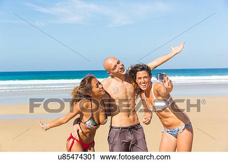 Man and two young women wearing swimwear taking camera selfie on beach, El Cotillo, Fuerteventura, Spain View Large Photo Image Stock Image - Man and two young women wearing swimwear taking camera selfie on beach, El Cotillo, Fuerteventura, Spain. Fotosearch